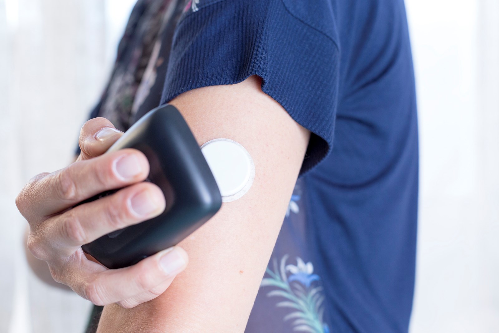 En kvinne med en Freestyle Libre sensor på armen skanner med avleseren for å få vite blodsukkernivået.