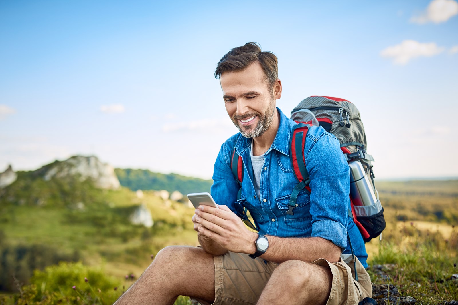 En mann på fjelltur ser på mobiltelefonen sin