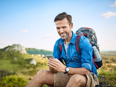 En mann på fjelltur ser på mobiltelefonen sin